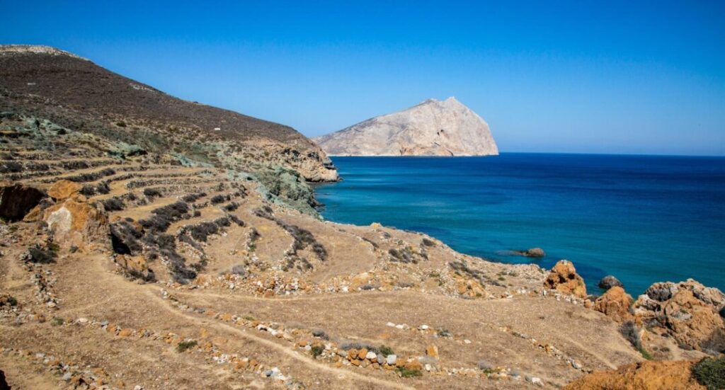 En el lado oriental de la isla, la roca Kalamos se erige como el segundo monolito calcáreo más alto del Mediterráneo, después de Gibraltar: una visita obligada para los alpinistas. A lo largo del día, la roca cambia de color con la cambiante luz del sol, lo que le confiere un aspecto singularmente llamativo. Al pie de la roca se encuentran el antiguo templo de Apolo y el monasterio de Zoodochos Pigi (Fuente: https://www.visit-anafi.gr/)